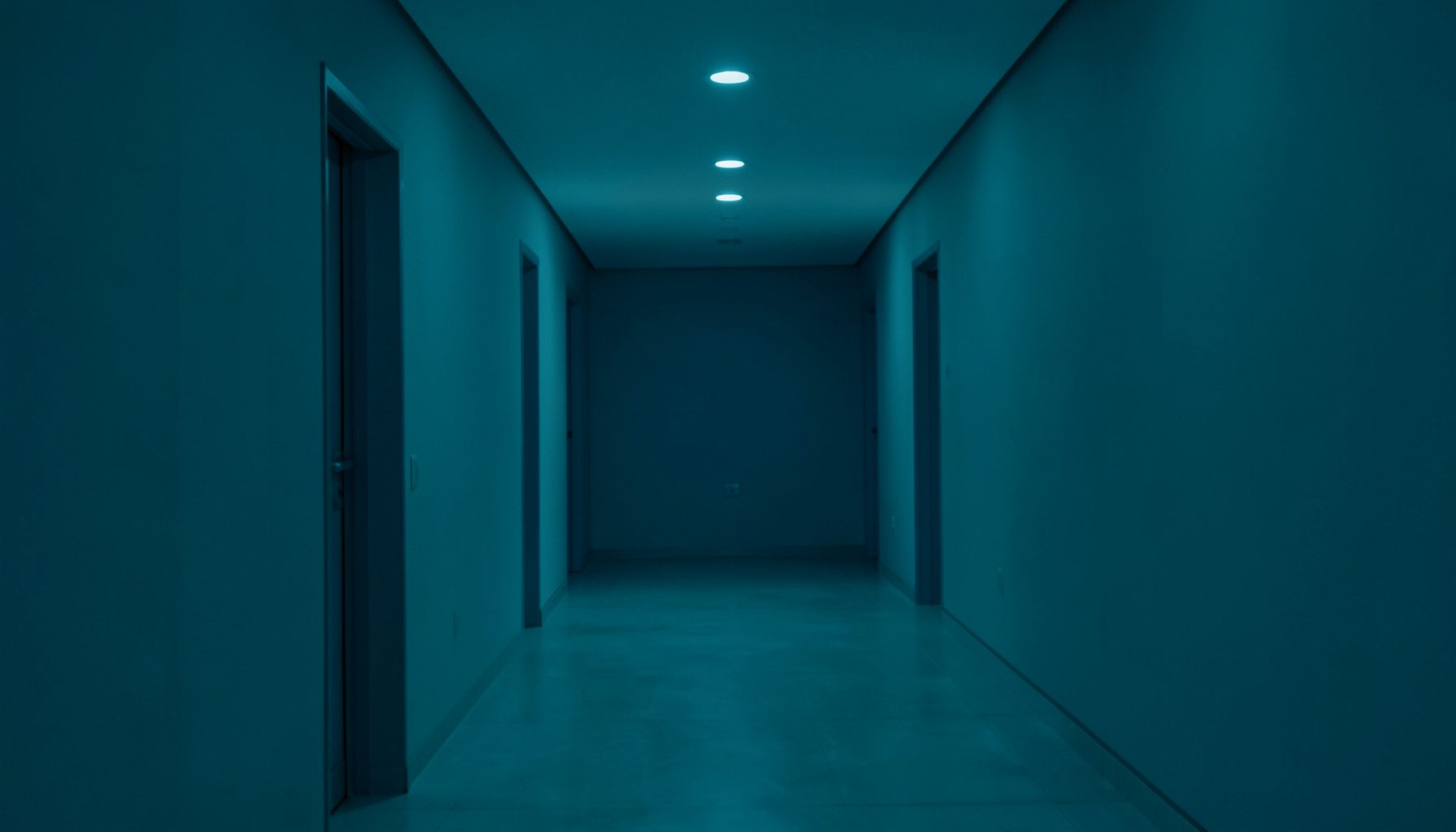Atmospheric photograph of a quiet, symmetrical interior hallway with soft overhead lighting and a calm teal tint