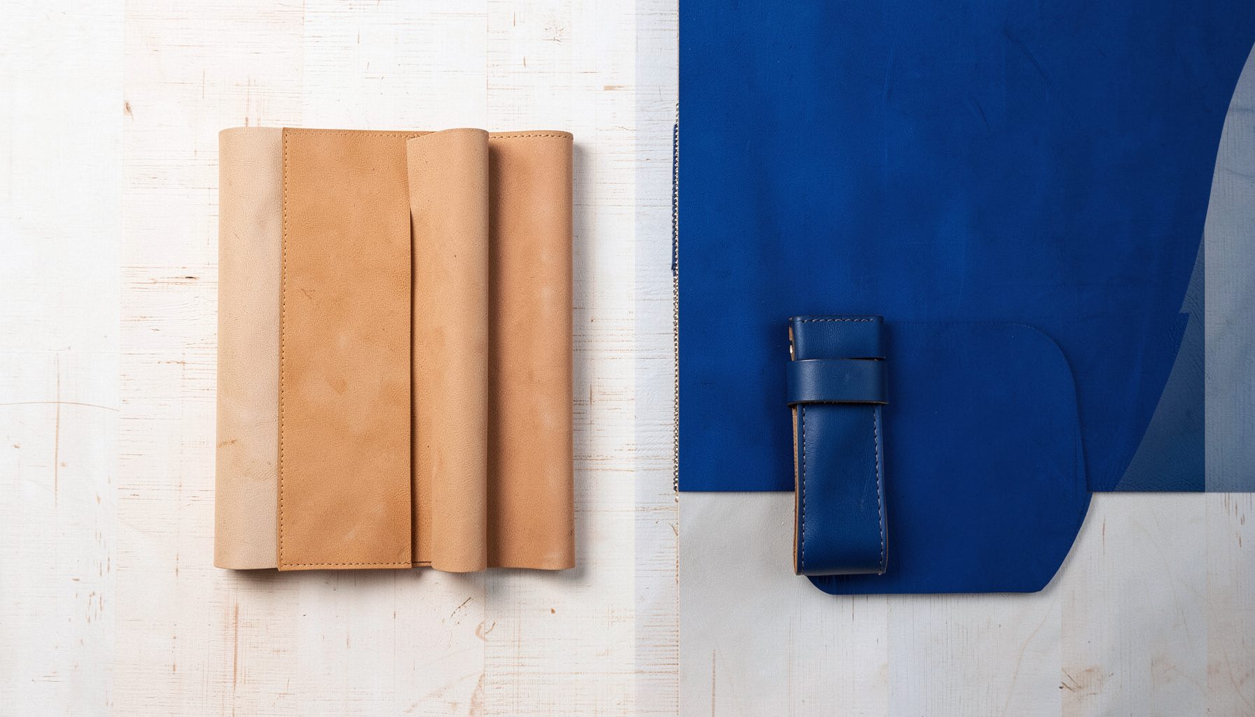 Flat lay arrangement of soft tan leather accessories on a pale wooden surface, lit by soft daylight