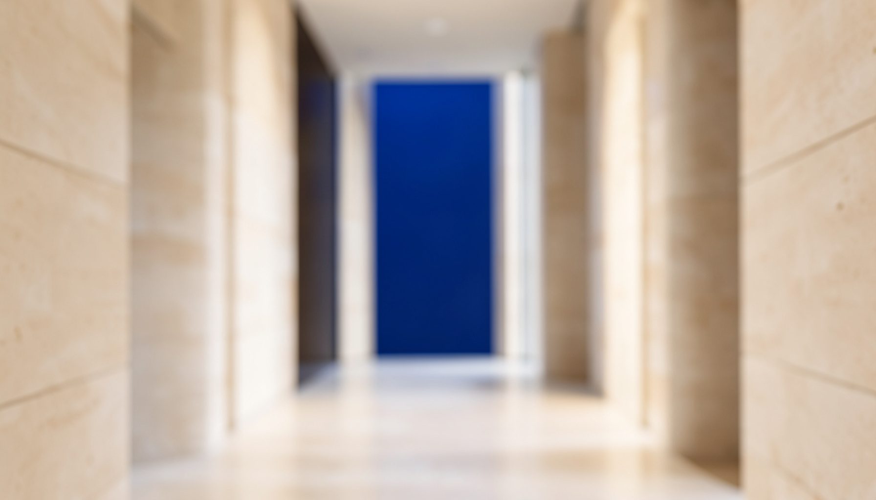 Symmetrical architectural photograph of a calm, softly blurred corridor with warm beige stone and gentle daylight, conveying quiet elegance