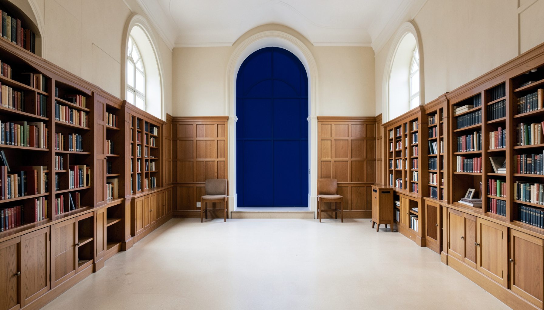 Symmetrical photograph of a quiet library reading room with tall arched windows, warm wood paneling, and neutral beige and cream tones
